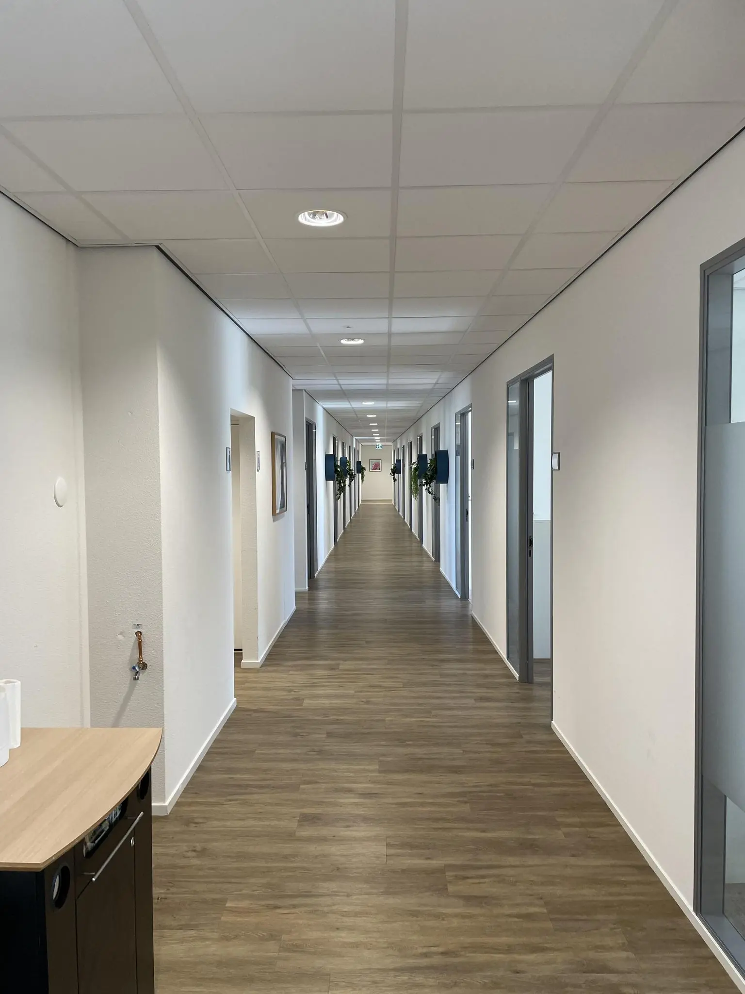 Lange, moderne gang met houten vloer en kantoren aan weerszijden in een gebouw aan de Johan Cruijff Boulevard.